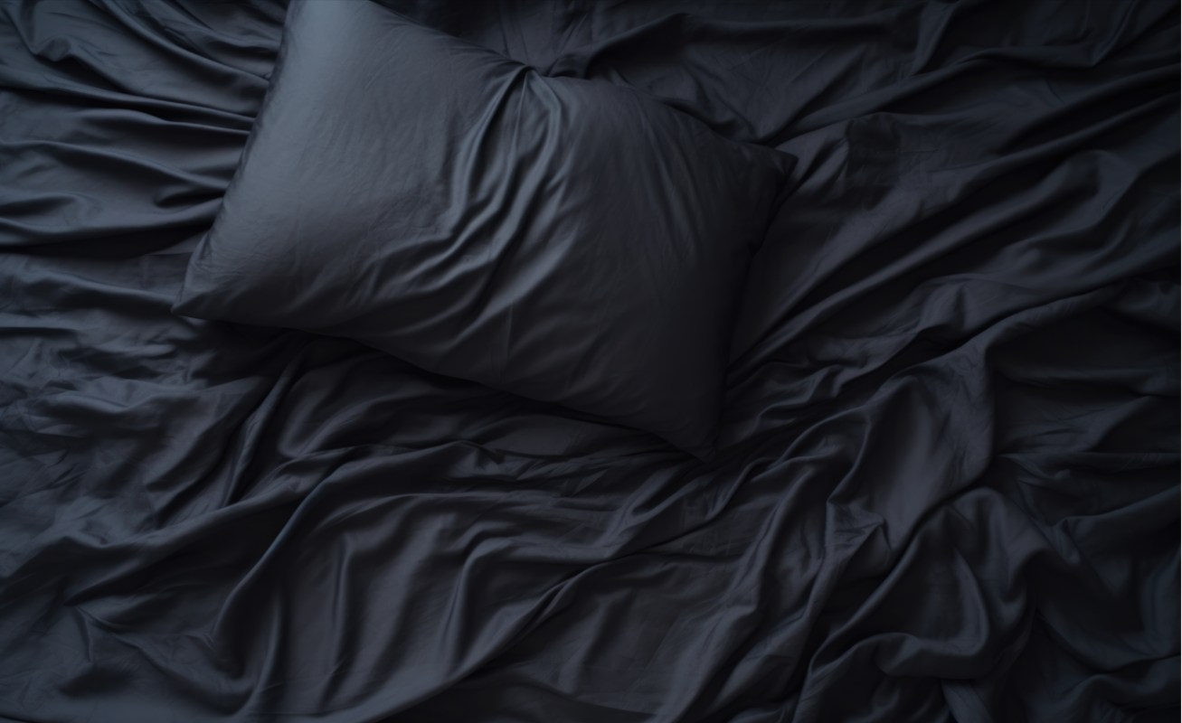 Dark gray crumpled bed sheets with a pillow on a bed, welcoming the sleeper to blissful, uninterrupted rest.